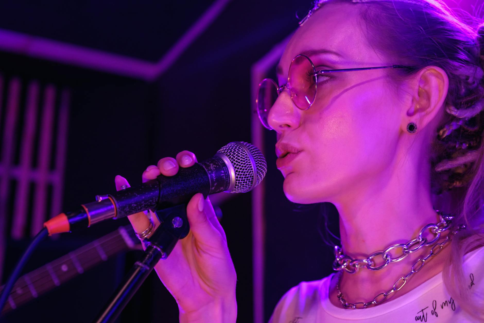 Close-up of a female vocalist wearing eyeglasses singing into a microphone on stage.