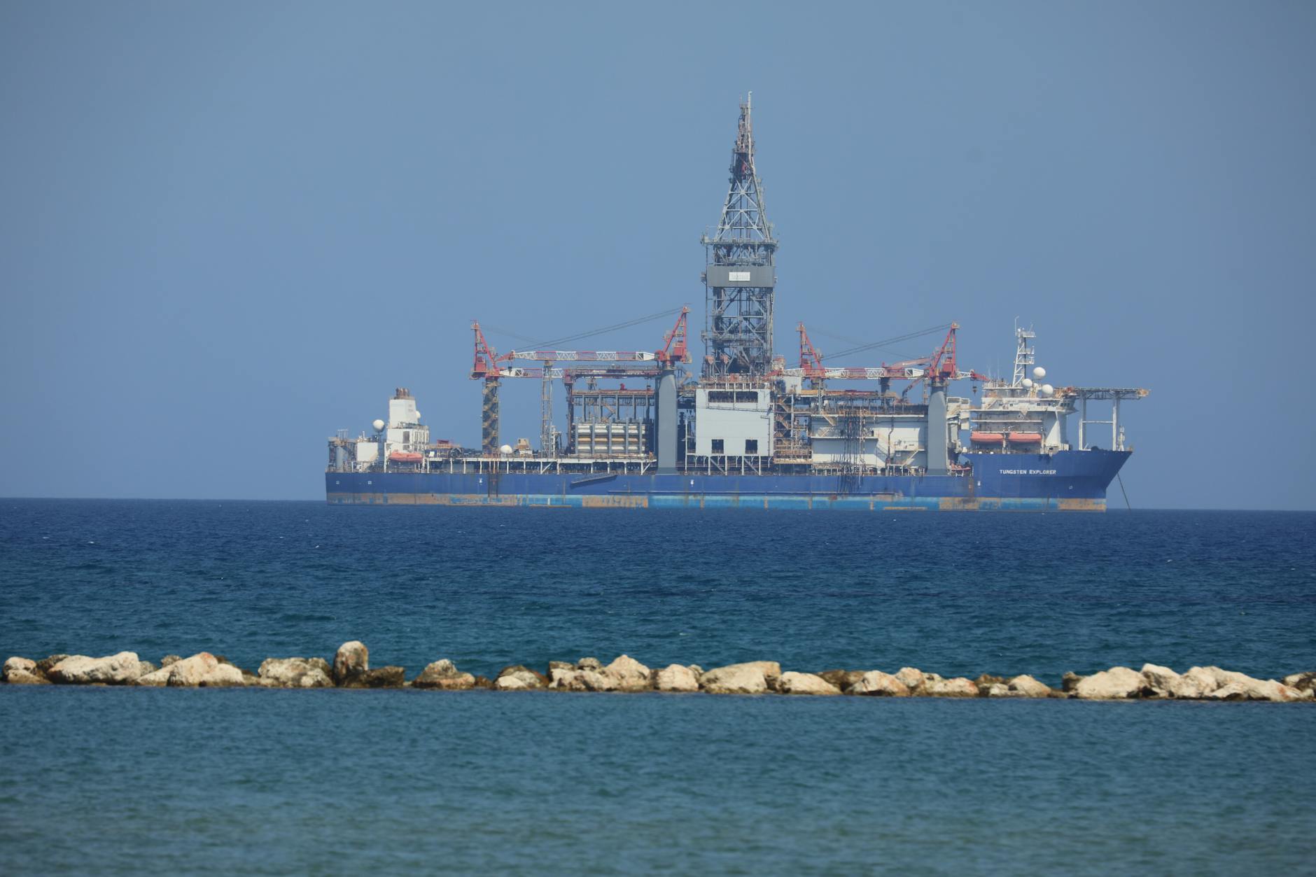 An offshore drilling rig floats on a calm sea with a clear blue sky in the background.