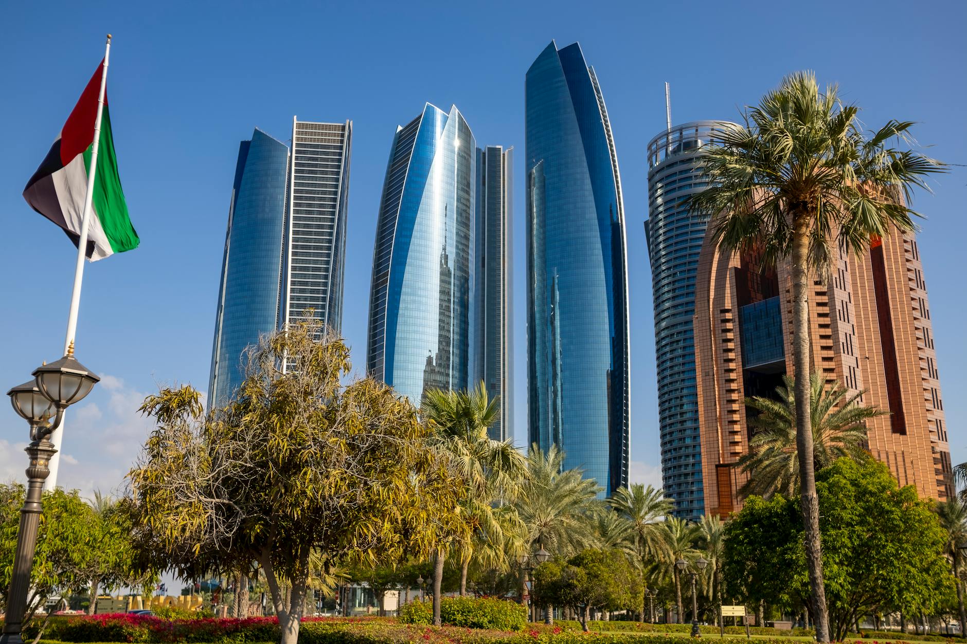 Captivating shot of the iconic Etihad Towers, Abu Dhabi landmark with palm trees and UAE flag.