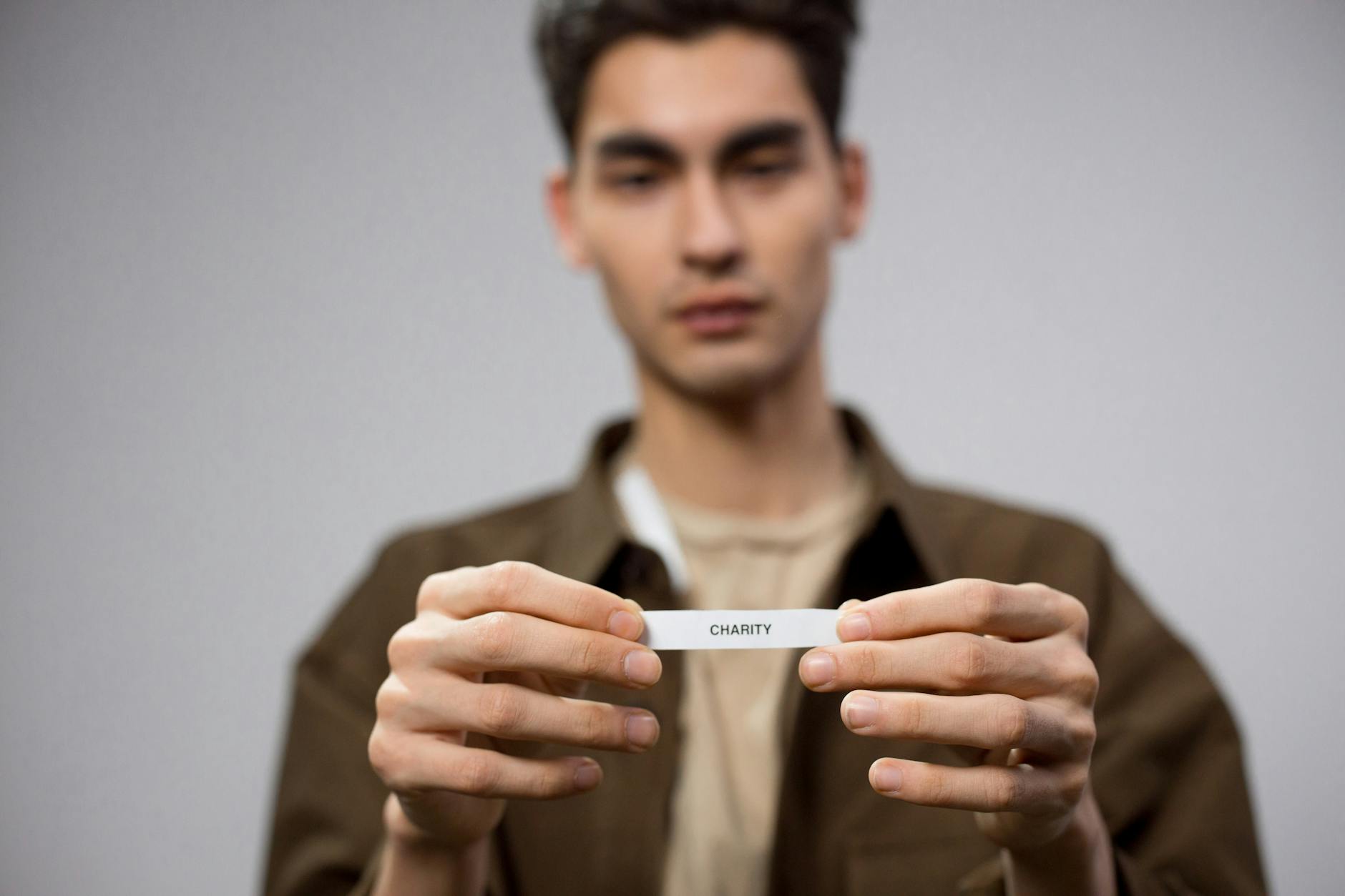 A man holds a note reading 'charity,' with the focus on his hands, expressing a charitable theme.