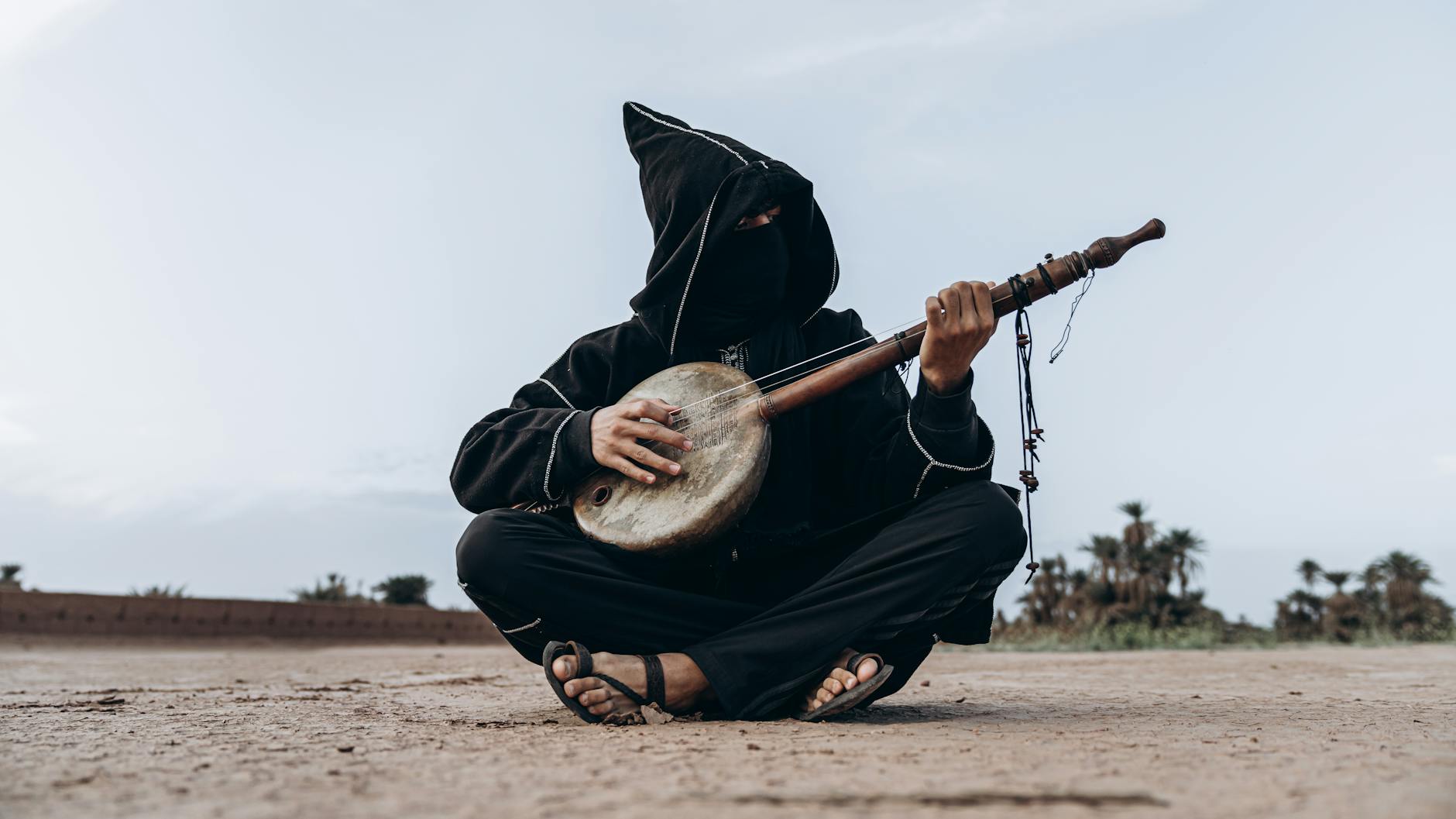 A masked musician plays an instrument in the Moroccan desert near Mhamid, reflecting cultural heritage.